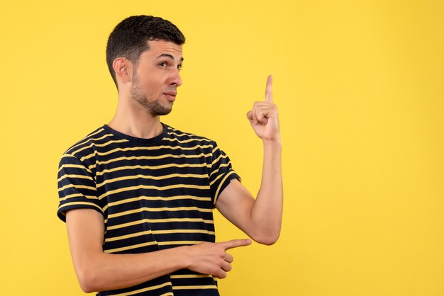 Вид спереди молодой человек в черно-белой полосатой футболке, стоящий на желтом изолированном фоне