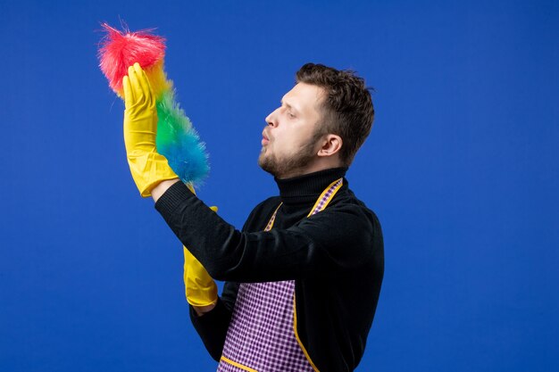 Front view of young man blowing on duster on blue wall