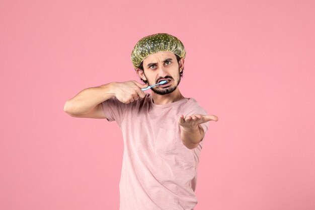 front view of young man brushing his teeth on pink wall