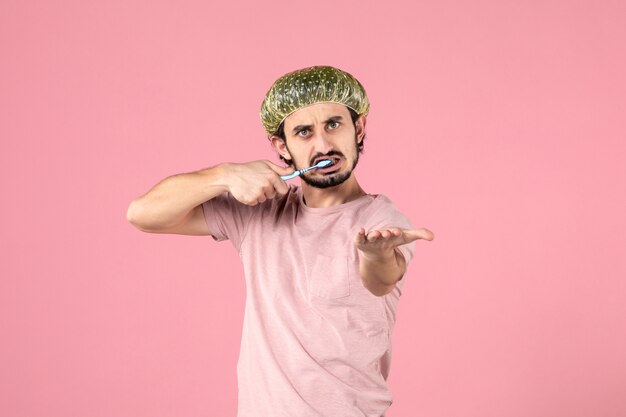 ピンクの壁に歯を磨く若い男の正面図