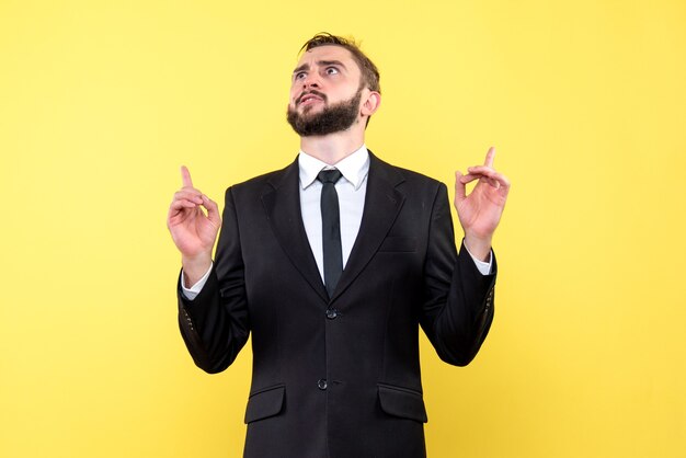 Front view of young man businessma with doubts pointing fingers up on yellow