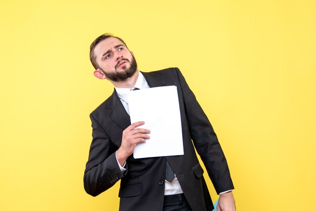 Front view of young man businessman bewildered looks aside and holdis document on yellow