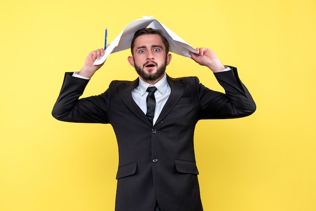 Front view of young man businessman going crazy touching head with blank paper sheets on yellow