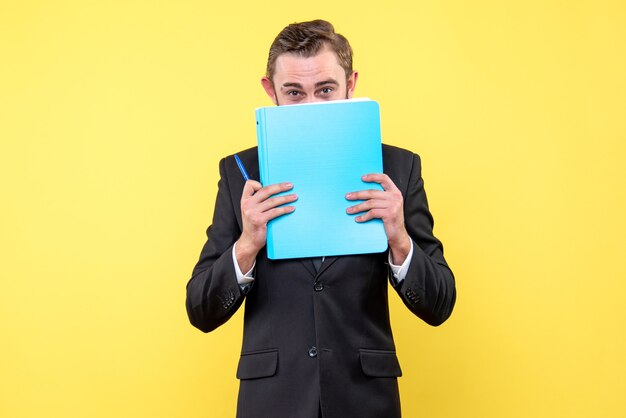 Front view of young man businessman hides the lower part of the face with the blue folder on yellow