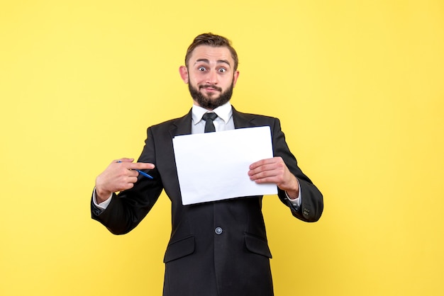 Front view of young man businessman looks surprised and points his forefinger to a blank paper on yellow