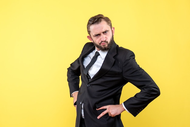 Front view of young man businessman outrageous holding hands on hips on yellow