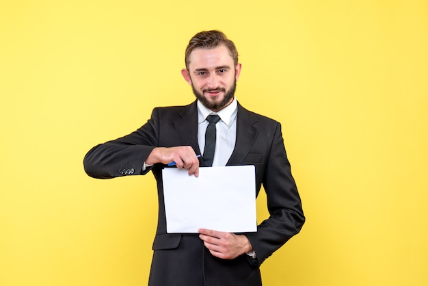 Front view of young man businessman in a suit smiling and holding blank paper in the center on yellow