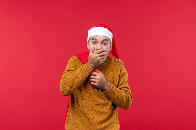 Front view of young man carrying present bag on red wall