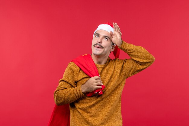 Front view of young man carrying red present bag on red wall