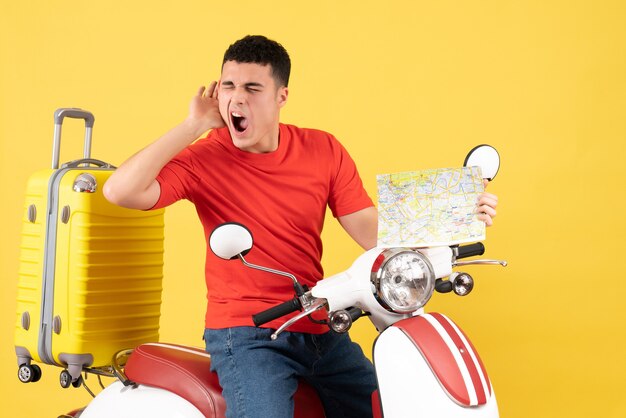 Front view young man in casual clothes on moped holding travel map listening to something