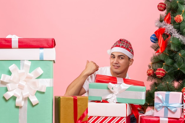 분홍색 벽에 선물 주위에 크리스마스를 축하하는 젊은 남자의 전면보기