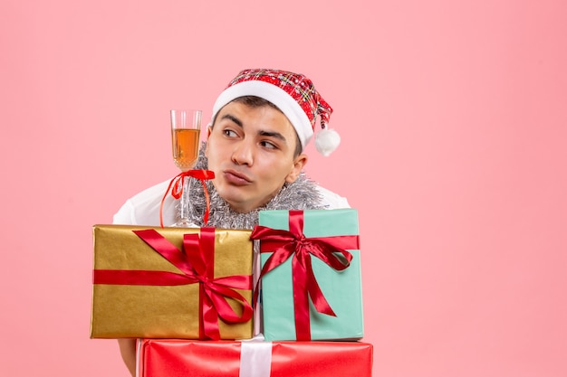 Front view of young man celebrating christmas around presents on pink wall