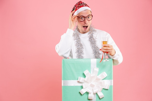 Front view of young man celebrating xmas with drink and garlands on pink wall