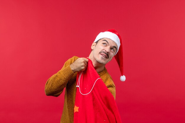 Front view of young man checking present bag on red wall