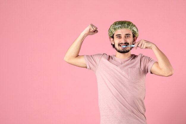 front view of young man cleaning his teeth and flexing on light pink wall