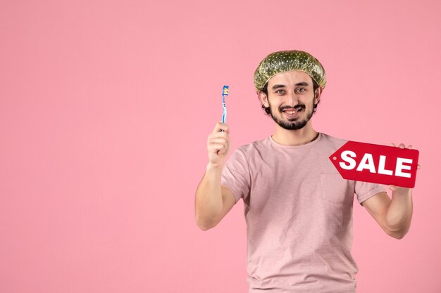 彼の歯を掃除し、ピンクの壁に販売バナーを保持している若い男の正面図