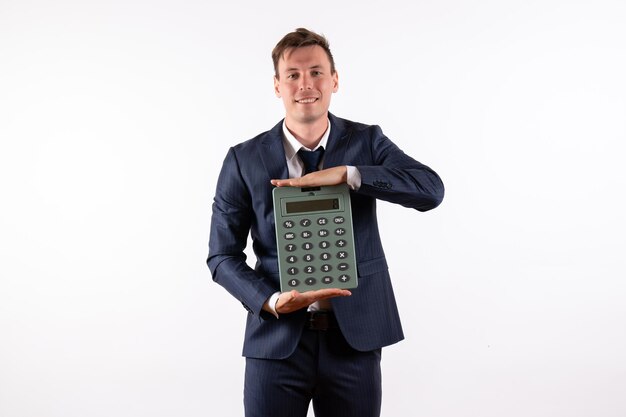 Front view young man in elegant classic suit holding huge calculator on a white background