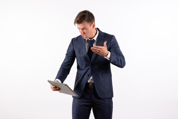 Front view young man in elegant classic suit holding huge calculator on white background