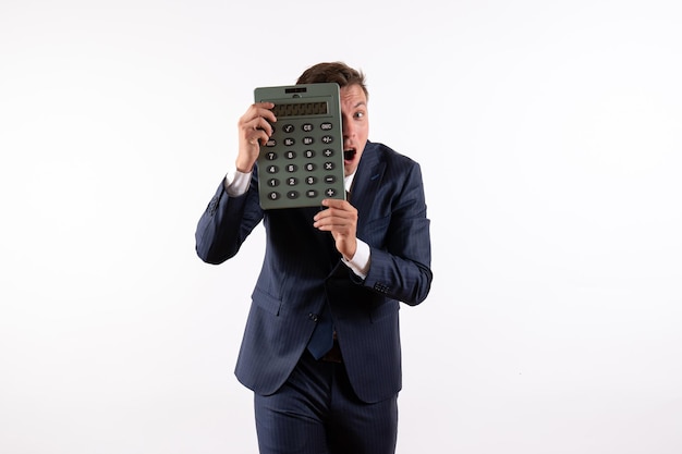 Front view young man in elegant classic suit holding huge calculator on white background