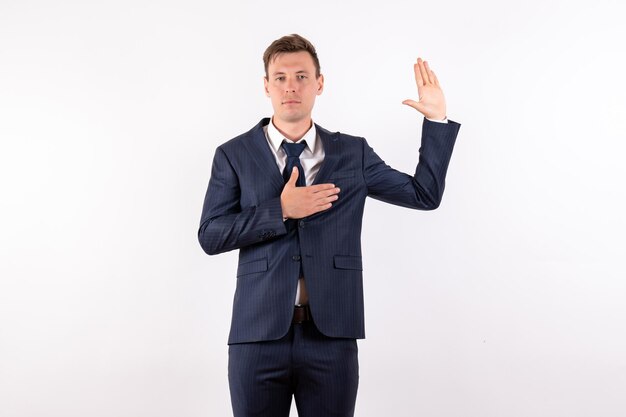 Front view young man in elegant classic suit raising his one palm on white background