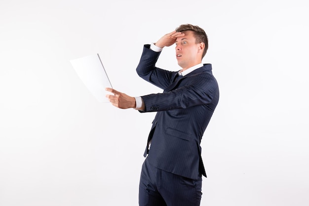 Front view young man in elegant classic suit reading documents on white background