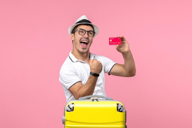 ピンクの壁に休暇中に感情的に銀行カードを保持している若い男の正面図