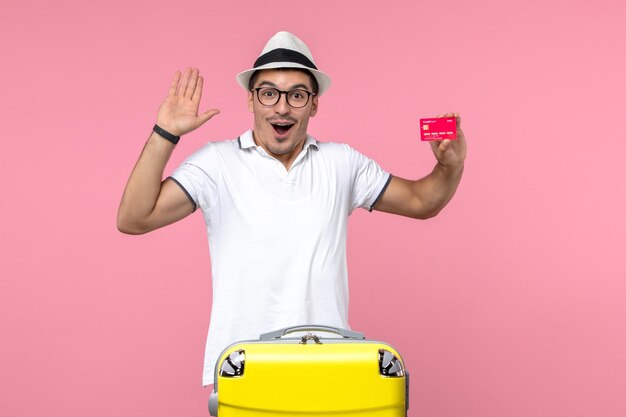 Front view of young man emotionally holding bank card on vacation on pink wall