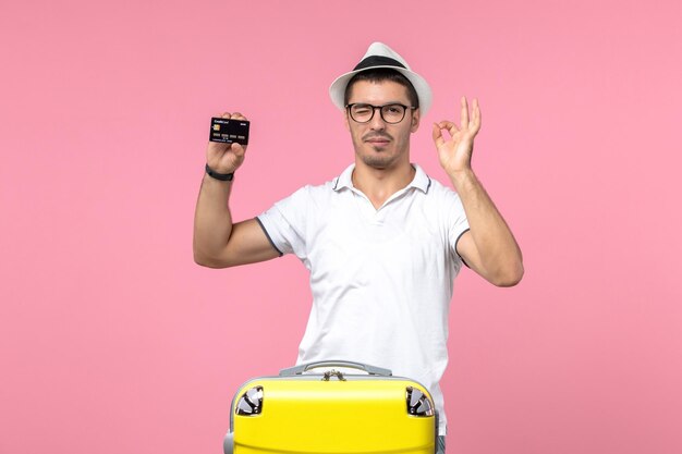 Front view of young man emotionally holding black bank card on a pink wall