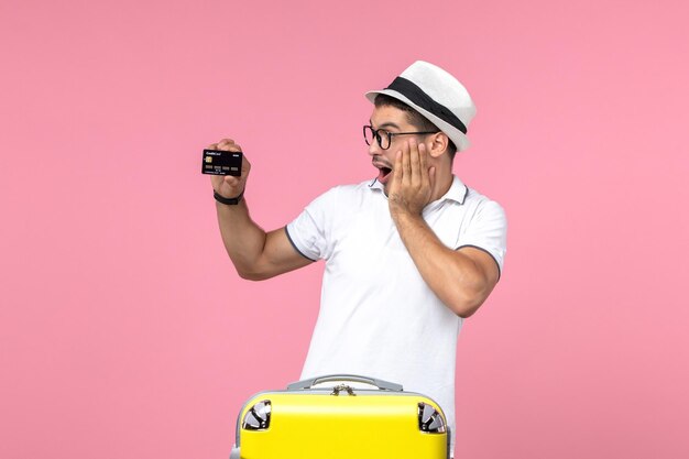 Front view of young man emotionally holding black bank card on pink wall