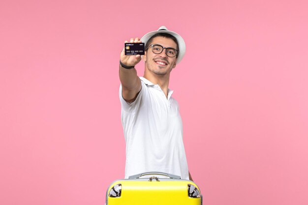 Вид спереди молодого человека, эмоционально держащего черную банковскую карту на розовой стене