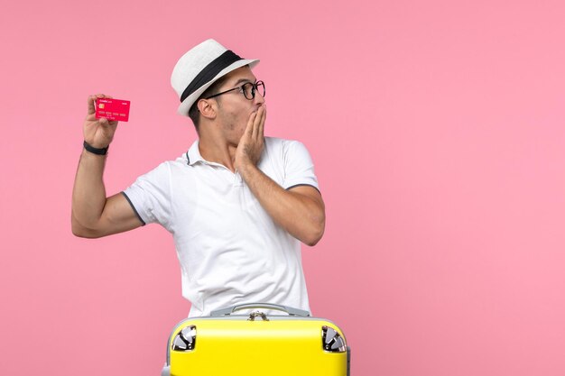 Вид спереди молодого человека, эмоционально держащего красную банковскую карту в отпуске на розовой стене