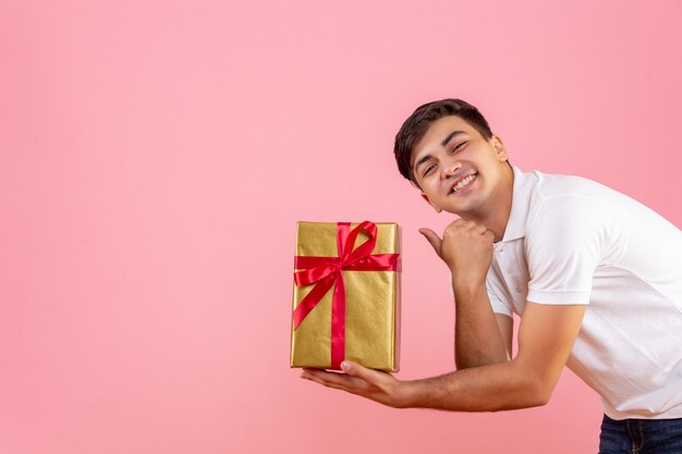Вид спереди молодого человека, дающего кому-то рождественский подарок на розовой стене
