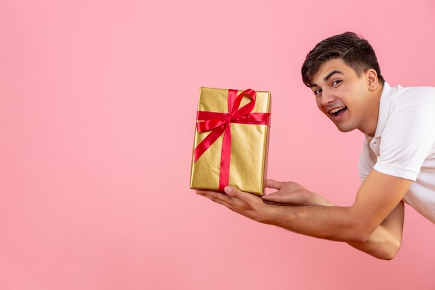 Front view of young man giving christmas present to someone on pink wall