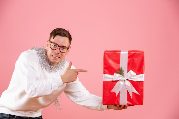 Front view of young man giving christmas present to someone on pink wall