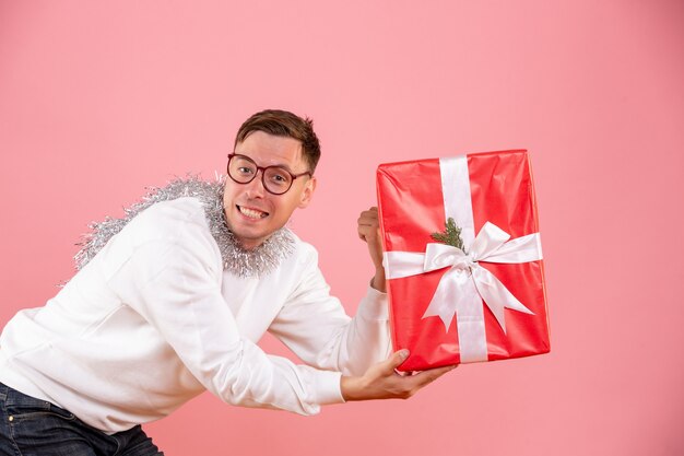 Front view of young man giving christmas present to someone on the pink wall