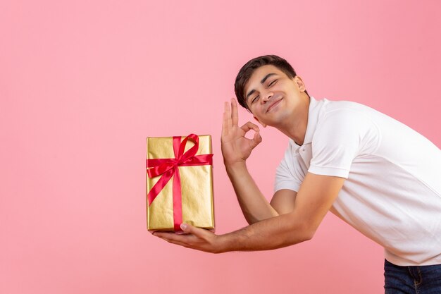 Front view of young man giving christmas present to someone on the pink wall