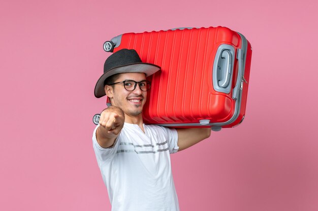 Вид спереди молодого человека, отправляющегося в отпуск и держащего красную сумку на розовой стене