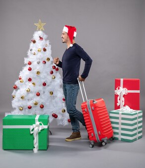 Вид спереди молодой человек идет с красным чемоданом на сером изолированном