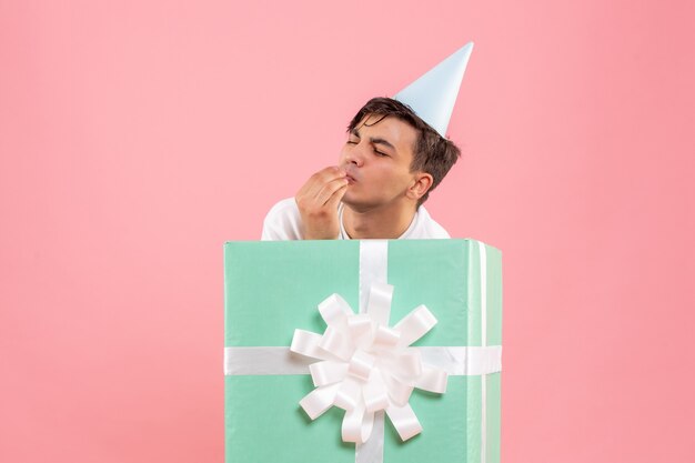 Front view of young man hiding inside present on a pink wall