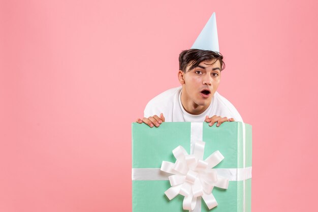 Front view of young man hiding inside present on pink wall