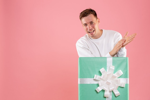 Front view of young man hiding inside present on pink wall