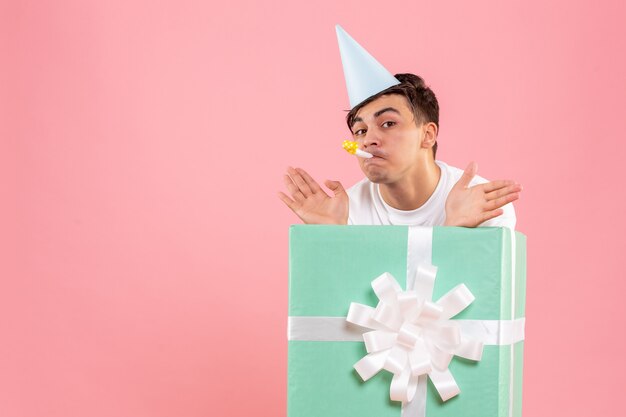 Front view of young man hiding inside present on pink wall