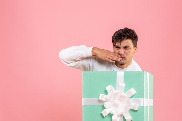 Front view of young man hiding inside present on the pink wall