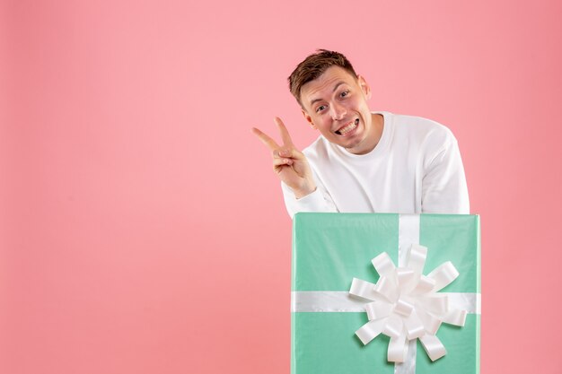 Front view of young man hiding inside present posing on pink wall