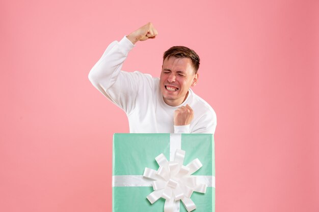 Front view of young man hiding inside present rejoicing on pink wall