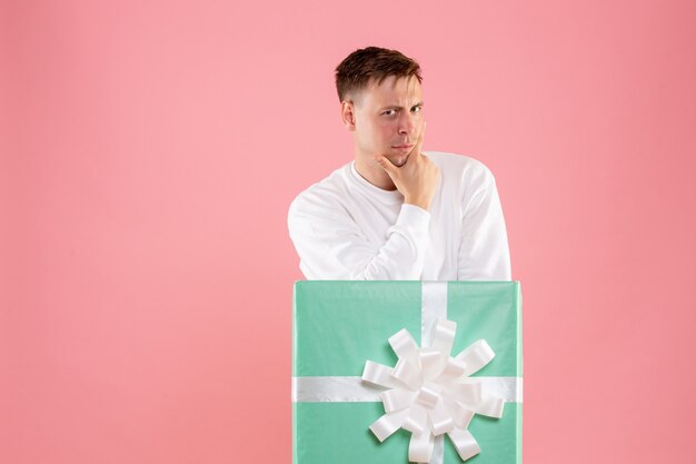 Front view of young man hiding inside present thinking on pink wall