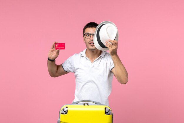 분홍색 벽에 은행 카드와 모자를 들고 있는 청년의 전면 모습