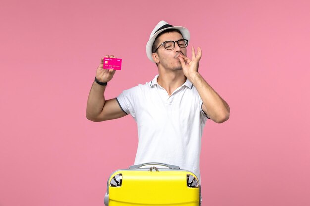 Front view of young man holding bank card on a pink wall