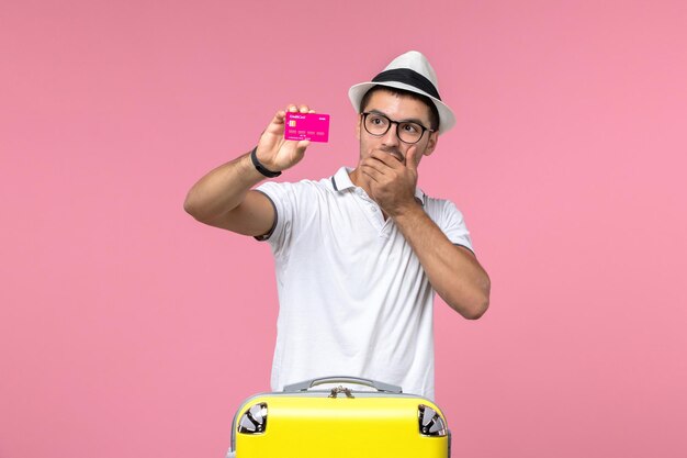 Front view of young man holding bank card on pink wall