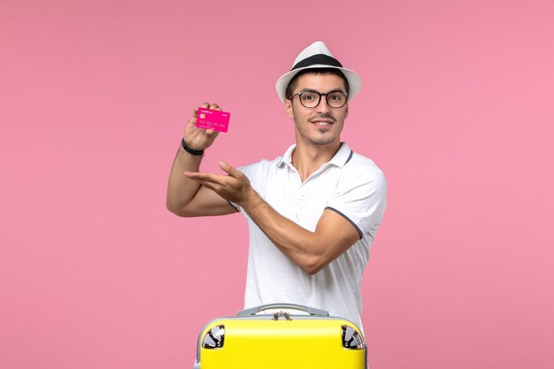 Front view of young man holding bank card on pink wall